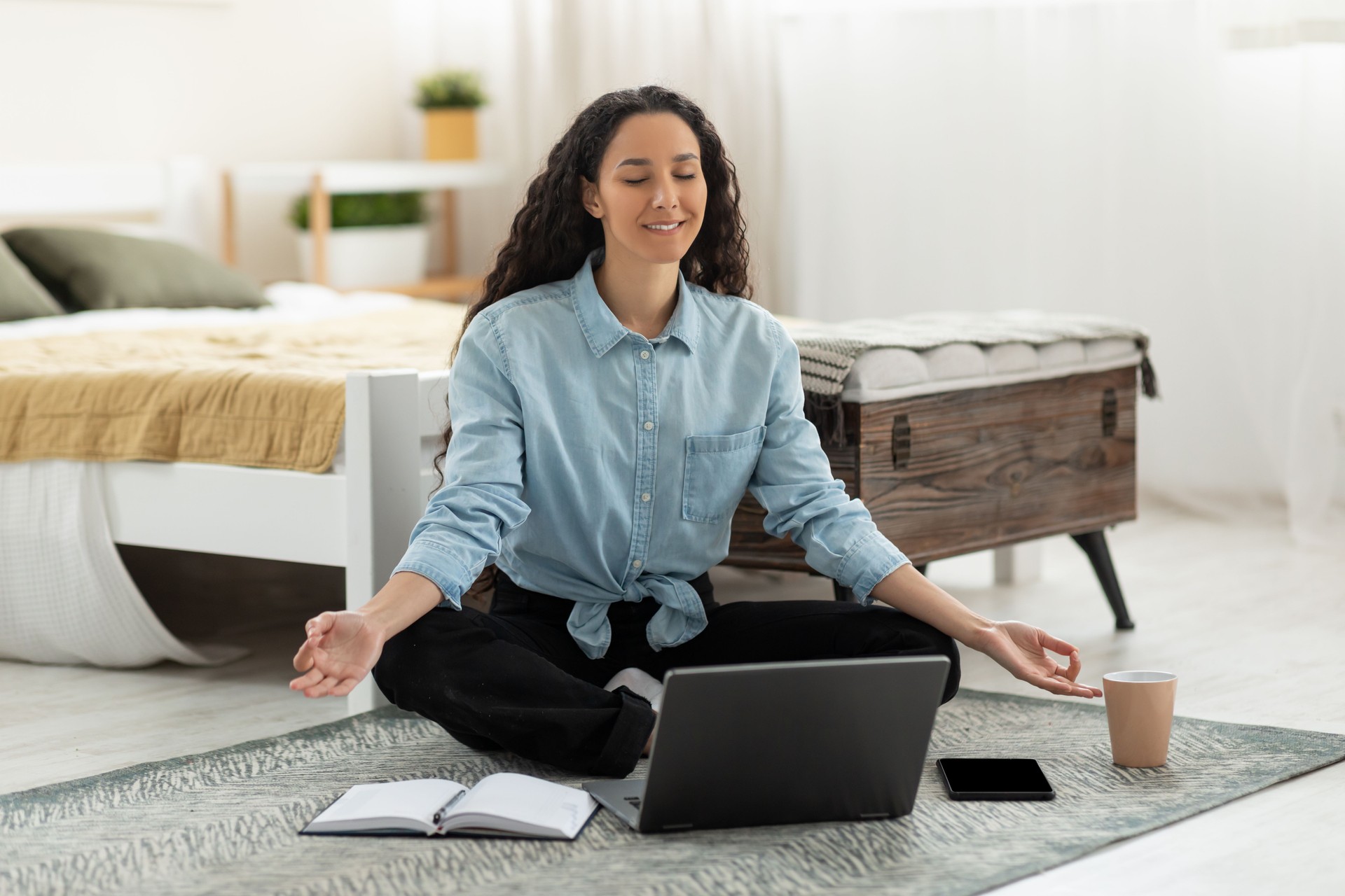 Young female freelancer meditating while working on laptop computer, sitting with eyes closed, relaxing at home office